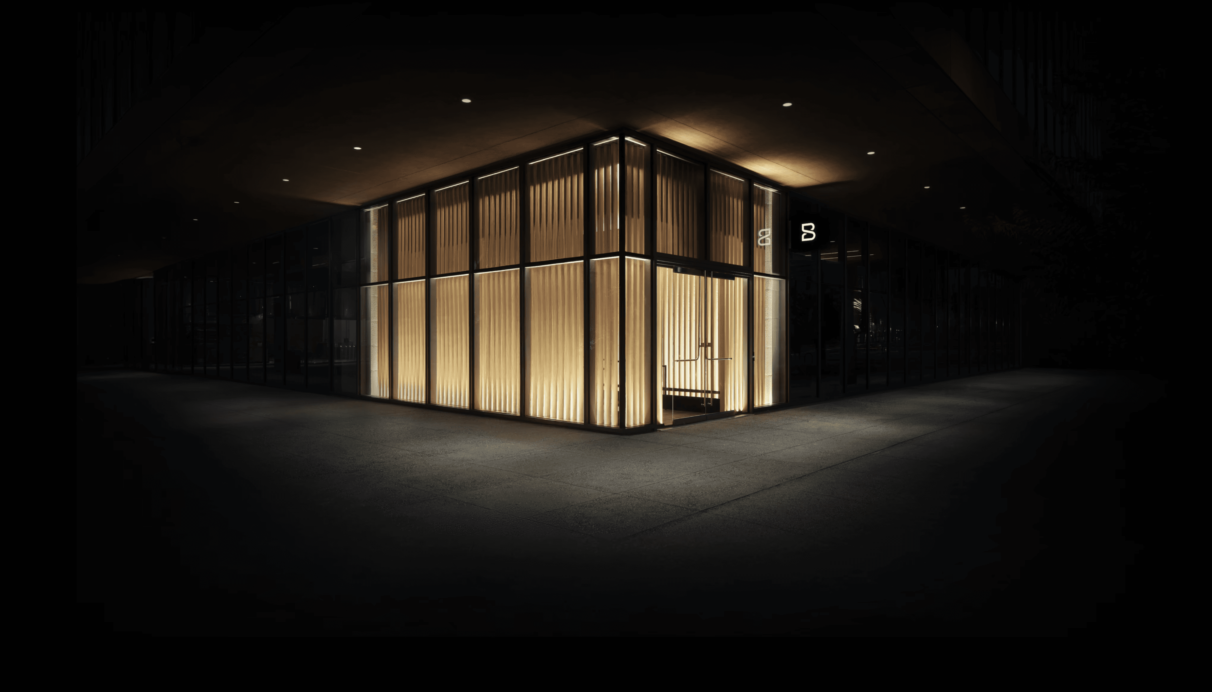 Biograph clinic exterior at night, a glass pavilion with vertical wood slats and warm interior lighting.